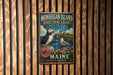A vintage metal sign for the Monhegan Island Bird Sanctuary in Maine, featuring a puffin and a seagull, is displayed on a wooden wall.