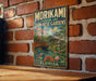 A vintage metal sign for the Morikami Museum and Japanese Gardens in Florida, featuring a scenic illustration of a Japanese garden with a bridge and cherry blossom trees.