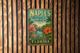 A vintage-style metal sign for the Naples Botanical Garden in Florida, featuring colorful tropical flowers and palm trees.