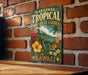 A vintage-style metal sign with the text "NATIONAL TROPICAL GARDEN" and "HAWAII" is displayed on a brick wall.