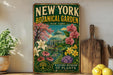 A vintage-style metal sign for the New York Botanical Garden, featuring a colorful illustration of a greenhouse surrounded by flowers and plants.
