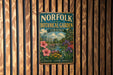 A vintage-style metal sign for the Norfolk Botanical Garden in Virginia, featuring a lush garden scene with flowers, plants, and a greenhouse.