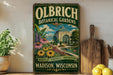 a vintage-style sign for Olbrich Botanical Gardens in Madison, Wisconsin, with a garden scene and a building in the background.