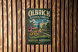 A vintage-style metal sign for Olbrich Botanical Gardens in Madison, Wisconsin, featuring a garden scene with flowers and a building.