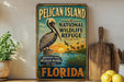 A vintage-style sign for the Pelican Island National Wildlife Refuge in Florida, featuring an illustration of a pelican and a sunset over the water.