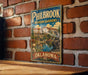 A vintage-style metal sign for Philbrook Museum Gardens in Oklahoma, featuring a scenic illustration of a garden with a statue and a building in the background.