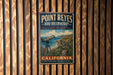 A vintage metal sign for Point Reyes Bird Observatory, featuring a telescope and a bird, mounted on a wooden wall.