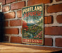 A vintage-style metal sign with the text "PORTLAND JAPANESE GARDEN OREGON" displayed on a brick wall.