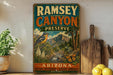 a vintage-style metal sign for Ramsey Canyon Preserve, with a bird and natural scenery on the sign. The sign is displayed on a shelf next to a wooden cutting board and a potted plant.