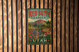 A vintage-style metal sign for the Red Butte Garden in Utah, featuring a scenic landscape with mountains, flowers, and a winding path.