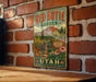 A vintage-style metal sign for the Red Butte Garden in Utah, featuring a scenic illustration of a garden path surrounded by colorful flowers and plants.