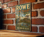 A vintage-style metal sign for the Rowe Sanctuary in Audubon, Nebraska, featuring an illustration of a bird and a wooden structure.