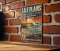 A vintage-style metal sign for the Salt Plains National Wildlife Refuge in Oklahoma, featuring an illustration of a bird and a sunset landscape.