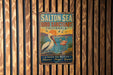 A vintage metal sign for the Salton Sea Bird Sanctuary in California, featuring a seagull and flamingos, is displayed on a wooden wall.