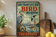 A vintage-style metal sign for the San Francisco Bay Bird Observatory in California, featuring illustrations of various bird species and the Golden Gate Bridge.