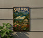 A vintage-style metal sign for Shelburne Museum Gardens in Vermont, featuring a scenic landscape with a building, flowers, and greenery.