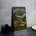 A vintage-style metal sign for Shore Acres State Park Garden in Oregon, featuring a scenic landscape with flowers and a body of water.
