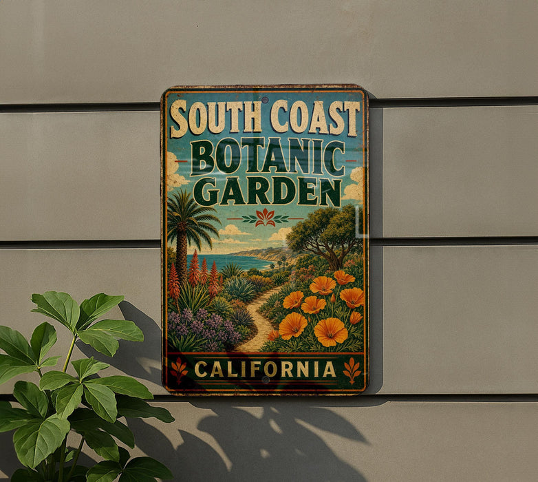 A vintage-style metal sign for the South Coast Botanic Garden in California, featuring a tropical garden scene with palm trees, flowers, and a winding path.