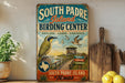 A vintage-style sign for the South Padre Island Birding Center, featuring a bird illustration and a wooden sign with the text "South Padre Island Birding Center" and "South Padre Island, Texas".