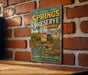 A vintage-style metal sign for Springs Preserve, Nevada, mounted on a brick wall.
