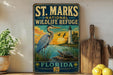 A vintage-style sign for St. Marks National Wildlife Refuge in Florida, featuring a large blue heron and a lighthouse in the background.