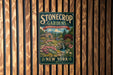 A vintage-style metal sign for "Stonecrop Gardens" in New York, featuring a garden scene with a house and flowers.