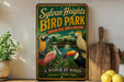 A vintage-style metal sign for Sylvan Heights Bird Park, featuring illustrations of various colorful birds in a tropical setting.