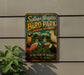 A vintage-style metal sign for Sylvan Heights Bird Park, featuring colorful illustrations of various bird species, is displayed on a wall next to a plant.