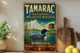 A vintage-style sign for the Tamarac National Wildlife Refuge in Minnesota, featuring a loon and a wooden cabin in a lake setting.