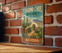 A vintage-style metal sign for Tohono Chul Park, featuring a desert garden oasis landscape with cacti, flowers, and a white archway entrance.