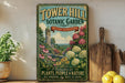 A vintage-style metal sign for Tower Hill Botanic Garden in Boston, Massachusetts, featuring a castle and colorful flowers, placed on a wooden shelf next to a potted plant and a cutting board.
