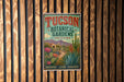 A vintage-style sign for the Tucson Botanical Gardens in Arizona, featuring a desert landscape with cacti, flowers, and mountains.