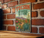 A vintage-style metal sign for the Tucson Botanical Gardens in Arizona, featuring a desert landscape with cacti, flowers, and mountains.