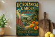 a vintage-style metal sign for UC Botanical Garden in Berkeley, California, with a lush garden scene and a bell tower in the background.