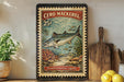 A vintage-style poster of a fish, likely a mackerel, is displayed on a wall next to a wooden cutting board and some kitchen utensils.