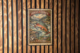 A vintage postage stamp featuring a fish, likely a trout, is displayed on a wooden wall.