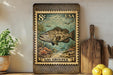 A framed postage stamp depicting a large fish, likely a gag grouper, is displayed on a shelf next to a wooden cutting board and some kitchen utensils.