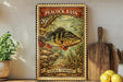 A framed vintage postage stamp featuring a peacock bass, with a price of 20 cents, is displayed on a shelf next to a wooden cutting board and a potted plant.