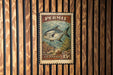 A vintage U.S. postage stamp featuring a fish on a coral reef, mounted on a wooden wall.