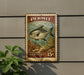 A vintage-style U.S. postage stamp featuring a fish illustration, mounted on a wall next to a plant.