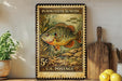 A vintage U.S. postage stamp featuring a pumpkinseed sunfish, displayed on a wooden shelf next to a wooden cutting board and a potted plant.