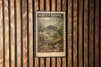A U.S. postage stamp featuring a fish, specifically a White Crappie, is displayed on a wooden wall.