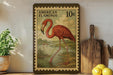 A framed stamp depicting an American flamingo, with a price of 10 cents, is displayed on a shelf next to a wooden cutting board and some lemons.
