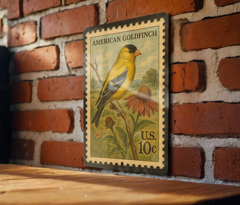 A vintage American Goldfinch postage stamp is displayed on a brick wall, featuring a yellow bird perched on a flower.