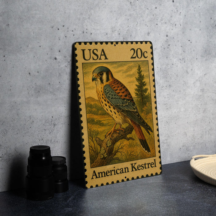 A framed American Kestrel postage stamp is displayed on a table, with a stack of black camera lenses and a white dish visible to the side.