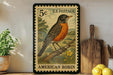 A vintage U.S. postage stamp featuring an illustration of an American robin perched on a branch, with a wooden cutting board and a potted plant in the background.