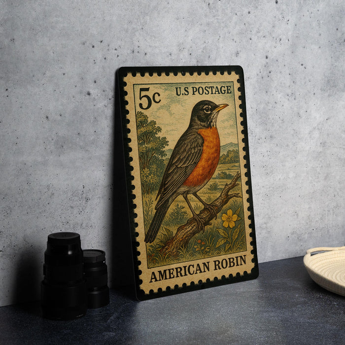 A U.S. postage stamp featuring an illustration of an American robin, placed on a countertop next to some black camera lenses.