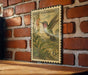 A vintage postage stamp featuring a colorful illustration of a hummingbird perched on a flower, mounted on a brick wall.