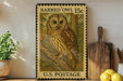 A vintage postage stamp featuring an illustration of a barred owl, with the text "BARRED Owl 15c" and "U.S. POSTAGE" printed on it. The stamp is displayed on a shelf next to a wooden cutting board and a potted plant.