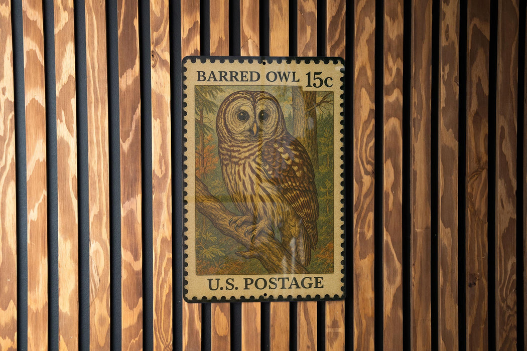 A U.S. postage stamp featuring a Barred Owl, which is a type of owl species, is displayed on a wooden background.